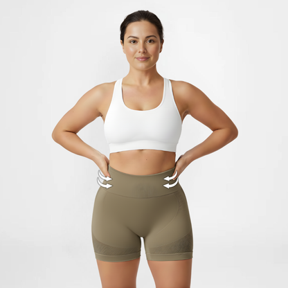 Woman wearing a white sports bra and olive green shorts on a light gray background